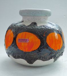 a white and black vase with orange dots on it