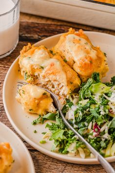 a white plate topped with lasagna covered in cheese next to a bowl of salad