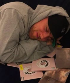 a man sleeping on top of papers with his head resting on his hands and eyes closed