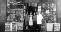 an old photo of three people standing in front of a store with posters on the wall