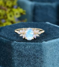 an opal stone ring sits on top of a blue velvet box with flowers in the background