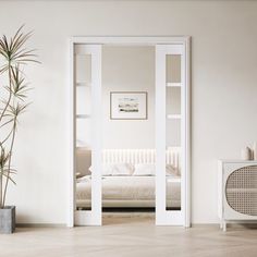 an empty room with a white bed and potted plant next to the door that is open