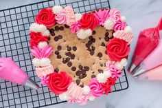 a heart shaped cookie with pink and white frosting on a cooling rack next to other baking utensils