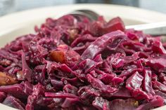 a white bowl filled with red cabbage on top of a table next to silverware