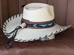 The Maverick starts with a Mexican soft palm leaf hat body that has a 3 3/4" brim and 5 1/4" crown. Hand laced in chocolate brown leather lace. The beaded hatband has a Thunderbird pattern and then mounted on distressed leather. The back of the band has a deer antler bead for accent. Starburst turquoise Concho and deep blue/green decorative feather completes the hat. All hats are made to order. Allow up to 4 weeks for your hat to ship. Western Style Brown Panama Hat With Flat Crown, Brown High Crown Fedora For Country Events, Western Brown Panama Hat With Flat Crown, Rustic High Crown Hat For Rodeo, Brown High Crown Fedora For Western-themed Events, Custom Flat Brim Straw Hat For Rodeo, Western High Crown Fedora In Brown, Brown High Crown Hat For Rodeo, Brown High Crown Hat For Western-themed Events