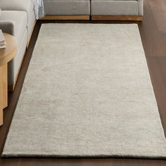 a living room with a couch, coffee table and white rug on the hardwood floor