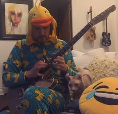 a man sitting on a bed playing a guitar with a dog in front of him