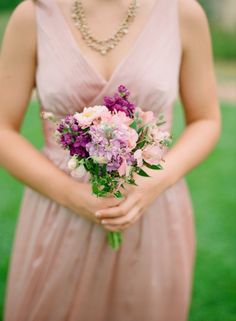 a woman in a pink dress holding a purple and white bouquet with pearls on her neck