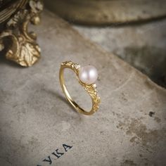 a gold ring with two pearls on it sitting on top of a stone slab next to a plant