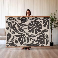 a woman is holding up a large black and white floral print on a wooden frame