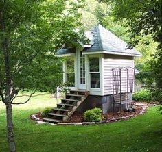 a small white shed sitting in the middle of a lush green field next to trees