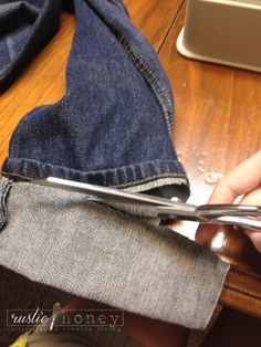 someone using scissors to cut through the back pocket of their jean pants on a wooden table