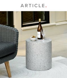 a bottle of wine sitting on top of a cement table next to a chair and window