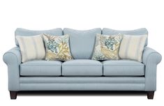 a light blue couch with two pillows on it's back and one pillow sitting on the arm