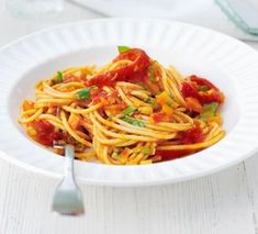 a white bowl filled with pasta and sauce on top of a table next to a fork