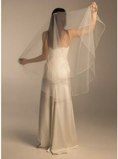 a woman in a white dress with a veil on her head and hands behind her back