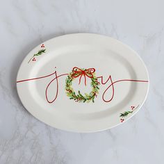 a white plate topped with a christmas wreath and the word joy painted on it's side