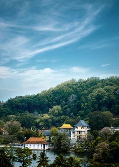 houses on the edge of a lake surrounded by trees and hills in the background with blue sky