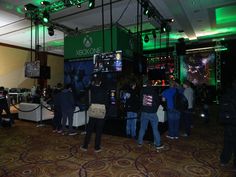 several people playing video games in a large room with green lights on the ceiling and carpeted floors