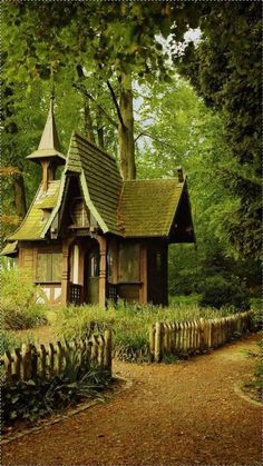 a small wooden house in the woods with a fence around it and trees on either side