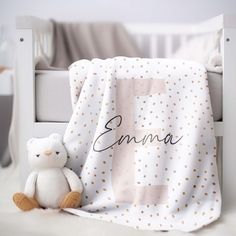 a white teddy bear sitting next to a blanket with the word's name on it