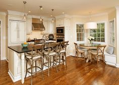 a large kitchen with white cabinets and wooden floors is shown in this image, there are several stools around the island