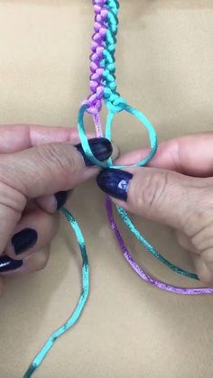 two hands are working on some colorful bracelets with blue, purple and green thread