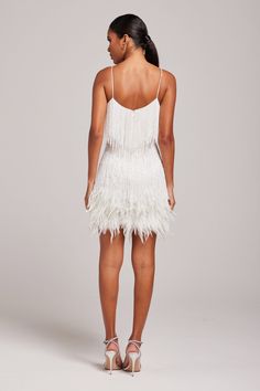 a woman wearing a white dress with feathers on the skirt and heels, back view