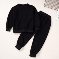 a black sweatshirt and sweatpants set on top of a white table next to a pair of scissors