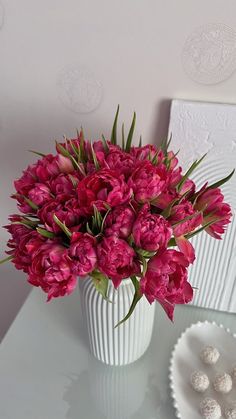 a white vase filled with pink flowers on top of a table next to a plate