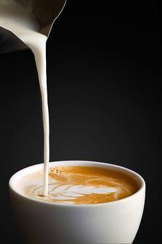 milk being poured into a white bowl filled with liquid on a black background in the dark