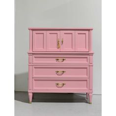 a pink dresser with two drawers and gold handles on the bottom, against a white wall