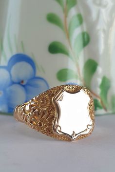 Glorious ornately engraved shoulders are the dream features of this solid gold vintage signet ring. The deeply engraved botanical designs along the shoulders create luxurious rich textures that contrast wonderfully against the simplicity of the shield and band.  The blank shield allows you to personalise the ring. Perhaps with your own initials, with initials of a loved one as a gift or memorial ring. Or, engraved with a date to celebrate a wedding or graduation. Personalising the ring will defi Luxury Gold Ring With Engraving Option, Luxury Vintage Oxidized Signet Ring, Luxury Yellow Signet Ring For Gift, Luxury Vintage Memorial Ring, Luxury Yellow Gold Memorial Ring, Ceremonial Gold Engraved Ring, Gold Engraved Signet Ring Collectible, Ceremonial Gold Engraved Ring With Engraving Option, Classic Gold Engraved Ring For Ceremonial Use