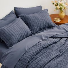 a bed with blue comforter and pillows on it next to a wooden side table