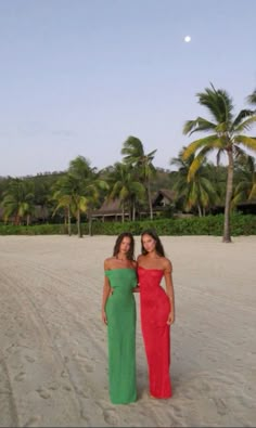 two women standing next to each other on top of a sandy beach with palm trees