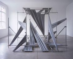 an art installation made out of metal rods and cloths in a white room with a large window