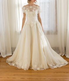 a woman standing in front of a window wearing a wedding dress with flowers on it