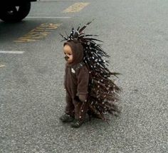 a small child dressed as a bear with spikes on his head is standing in the street