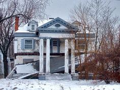 an old run down house with snow on the ground and trees in front of it