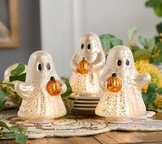 three white ghost figurines sitting on top of a table next to plates and flowers