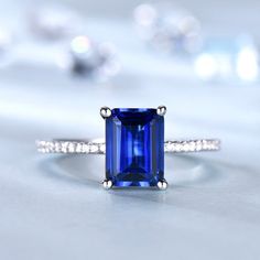 an emerald cut blue sapphire and diamond ring on a white surface with diamonds surrounding it