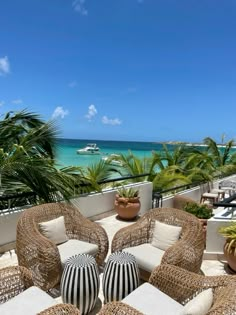 an outdoor seating area with wicker furniture and palm trees on the balcony overlooking the ocean