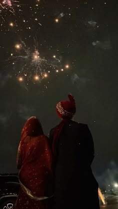 two people looking at fireworks in the sky with red and gold colors on their heads