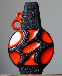 an orange and black glass vase sitting on top of a wooden table next to a gray wall