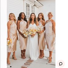 a group of women standing next to each other in front of a white building holding bouquets