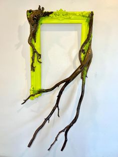 a green frame with branches hanging from it's sides in front of a white wall