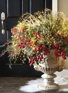 a vase filled with red berries and greenery on top of a wooden floor next to a black door