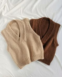 two knitted sweaters laying on top of a white bed next to each other