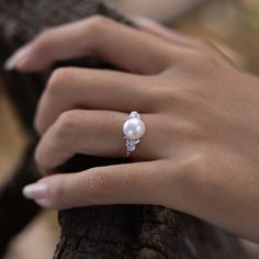 a close up of a person's hand with a pearl ring on her finger