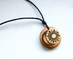 a wooden pendant with a sun and moon on it's side hanging from a black cord